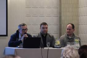 Pokaż zdjęcie: Przy stole konferencyjnym siedzi trzech mężczyzn przedstawicieli fundacji Ikar, jeden z mężczyzn trzyma mikrofon