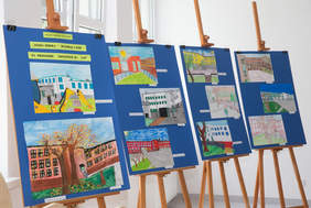 Pokaż zdjęcie: fragment pomieszczenia na czterech sztalugach są umieszczone rysunki uczniów przedstawiające budynek szkoły na przestrzeni 30 lati