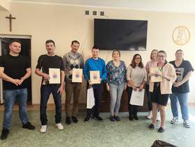 Dziewięć osób pozuje do pamiątkowego zdjęcia, trzymają przed sobą pamiątkowe dyplomy.