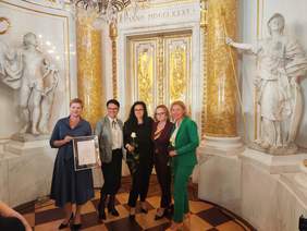 Pokaż zdjęcie: Do pamiątkowego zdjęcia pozuje pięć kobiet. Jedna z nich trzyma w ręku różę, inna prezentuje dyplom-nagrodę.