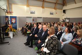 Pokaż zdjęcie: Uczestnicy konferencji siedzący na krzesełkach w sali gimnastycznej.