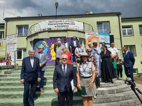 Pokaż zdjęcie: Przed budynkiem znajdują się schody, na których stoją ludzie. Nad nimi wisi transparent z napisem: Ogólnopolski Zlot Drużyn Nieprzetartego Szlaku ZHP w Stemplewie. 