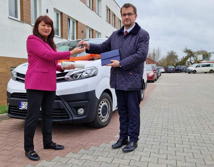 Pokaż zdjęcie: Dyrektor Oddziału PFRON w Zielonej Górze przekazuje kluczyki do nowego auta Dyrektor SOSW w Sulęcinie. Są na placu przed budynkiem, stoją tuż przed autem.