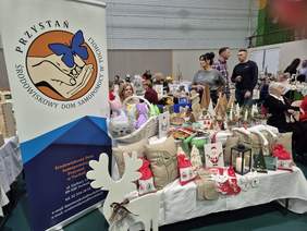 Stoisko ze świątecznymi wyrobami rękodzielniczymi. Po lewej stronie stoi baner ŚDS-u "Przystań" z Tucholi