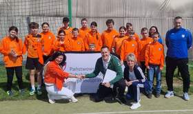 Zawodnicy oraz opiekunowie pozują do zdjęcia. Większość ubrana jest na pomarańczowo. Na soku zdjęcia widoczne logo PFRON.