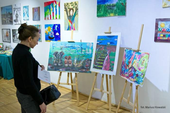 Pokaż zdjęcie: Kobieta w czarnym swetrze ogląda obrazy zaprezentowane podczas wystawy