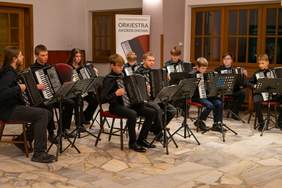 Pokaż zdjęcie: Zachodniopomorska Orkiestra Akordeonowa w trakcie występu. Grupa młodych muzyków grających na akordeonach w eleganckim wnętrzu, tworząc niepowtarzalną oprawę artystyczną wydarzenia.
