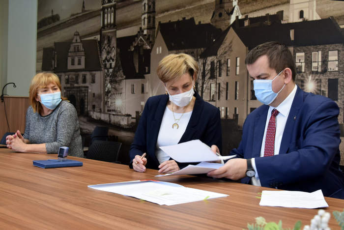 Pokaż zdjęcie: Dyrektor Oddziału Lubuskiego PFRON w trakcie podpisywania umowy przy stole wraz z przedstawicielami Powiatu Nowosolskiego na tle baneru promocyjnego Starostwa Nowosolskiego
