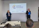 Oficjalne spotkanie w sali konferencyjnej na tle ekranu projekcyjnego z logo i napisem "Centrum Komunikacji dla Osób z Niepełnosprawnościami, Szczecin 9 czerwca 2026". Po lewej kobieta z w ciemnym garniturze ze złożonymi przed sobą rękoma. Po prawej mężczyzna w garniturze i okularach. 
