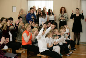 Pokaż zdjęcie: Dorośli i dzieci siedzący na krzesłach i słuchający wystąpienia