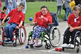 Pokaż zdjęcie: Trzy osoby na wózkach inwalidzkich grają w Boccia