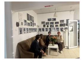 Pokaż zdjęcie: Przedstawiciele PFRON podczas spotkania z Marią Pietruszą-Budzyńską, prezeską Fundacji Teatroterapia Lubelska, w pomieszczeniu ozdobionym fotografiami dokumentującymi działalność teatru.