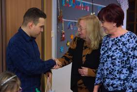 Pokaż zdjęcie: Dwie kobiety stoją obok siebie jedna z nich trzyma dłoń mężczyzny składa gratulacje.