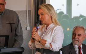 Pokaż zdjęcie: Kobieta w białej bluzce przemawia z mikrofonem w ręku