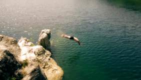 Chłopak skaczący na główkę ze skał do wody - ujęcie z wideoklipu zespołu Skołowani