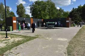 Pokaż zdjęcie: cztery kontenery mieszkalne, przed wejściem stoi grupa ludzi