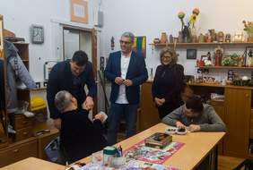 Pokaż zdjęcie: Wymiana uścisków dłoni dyrektora PFRON i uczestnika warsztatów. W pracowni artystycznej jest jeszcze jeden uczestników, który maluje, dyrektor WTZ oraz przewodnicząca PSONI w Giżycku