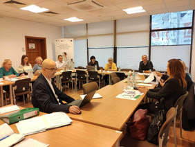 Pokaż zdjęcie: Sala, stoły utstawione w kształt podkowy. Za nimi siedzą członkowie Komisji, przed nimi dokumenty. 