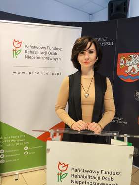 Pokaż zdjęcie: Młoda kobieta stoi przy mównicy.