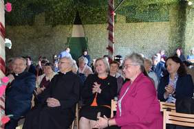 Pokaż zdjęcie: Pod namiotem na krzesełkach siedzą zaproszeni goście, spoglądają w kierunku sceny