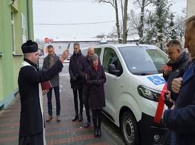 Pokaż zdjęcie: na zdjęciu biały bus został poświęcony przez księdza, obok stoją osoby i uczestniczą w uroczystym przekazaniu busa do ośrodka szkolno wychowawczego w Opocznie