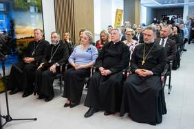 Pokaż zdjęcie: Przedstawiciele władz samorządowych i duchowieństwa siedzą w pierwszym rzędzie podczas uroczystości otwarcia Zakładu Aktywności Zawodowej w Sokółce, a w tle widoczni są pozostali goście wydarzenia.