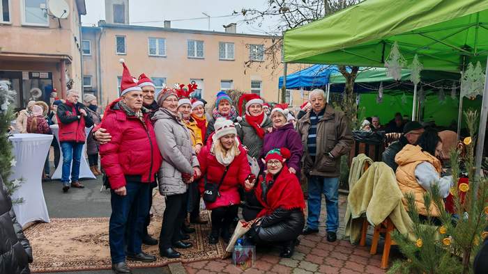 Pokaż zdjęcie: Grupa osób ubrana w stroje mikołajkowe i znajdująca się przed budynkiem DPS w Glińsku prezentuje się do zdjęcia