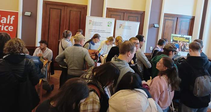 Pokaż zdjęcie: Grupa kilkunastu osób znajduje się w sali konferencyjnej i czeka w kolejce do poszczególnych wystawców, którzy mają swoje stoiska na Giełdzie Pracy. Po środku, przy stoisku Oddziału Wielkopolskiego PFRON można dostrzec dwa banery: PFRON oraz CIDON.