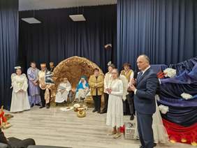 Szopka i postacie aktorów w centralnej części, z prawej mężczyzna w garniturze przemawia do mikrofonu