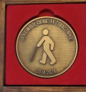 Jedna strona medalu: na środku postać z laską, nad nią napis Ja nie widzę Ciebie, Ty zobacz mnie. Po spodem: 2014 - 2024