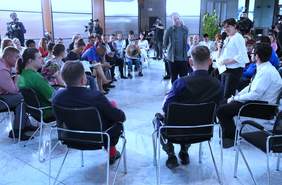 Pokaż zdjęcie: Zdjęcie z nagrania do prohramu autentyczni, pośrodku osób siedzących na krzesłach stoi Maciej Stuhr, z tyłu widać kamerzystów