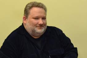 Pokaż zdjęcie: mężczyzna uśmiechnięty siedzi przy biurku