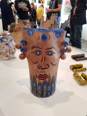 ceramika, prace uczestników, na pierwszym planie wazon-głowa, z tyłu widać fragmenty sylwetek osób