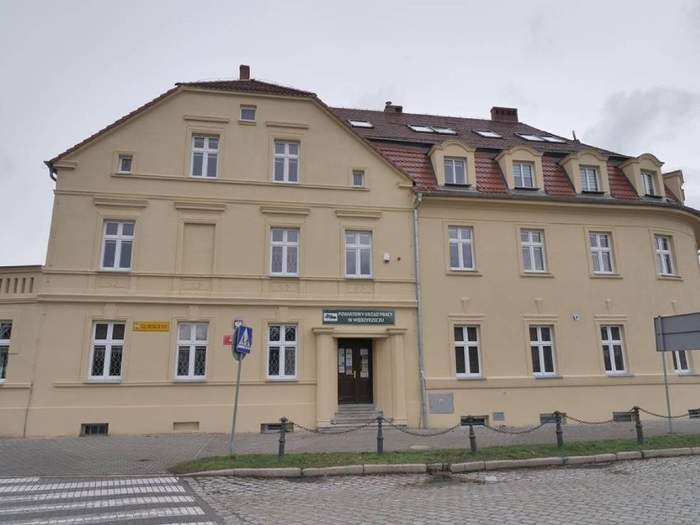 Pokaż zdjęcie: Budynek PUP w Międzyrzeczu, w kolorze beżowym, widać ulicę, jest pochmurno