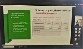 Zdjecie pulpitu monitora, na którym widoczny jest slajd ze spotkania online, z boku widoczne zdjęcie prowadzącego i ikonki osób uczestniczących w spotkaniu