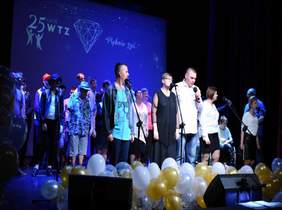 Pokaż zdjęcie: scena Miejskiego Ośrodka Kultury. gra świateł na środku stoją uczestnicy  WTZ i występują pokazując swoje talenty muzyczne i taneczne