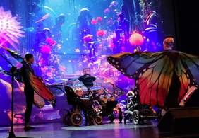 Pokaż zdjęcie: Taniec motyli - podopieczni stowarzyszenia w strojach motyli tańczą na scenie