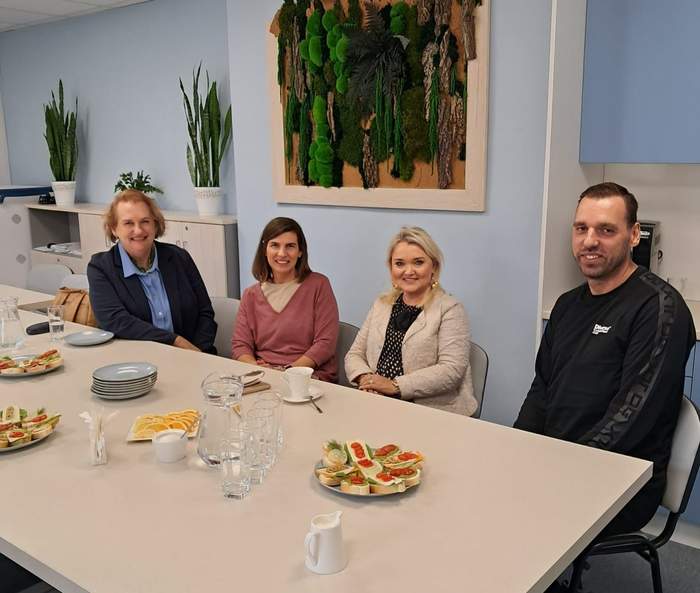 Pokaż zdjęcie: Dyrektorka Oddziału PFRON w Zielonej Górze siedzi przy stoliku z kawą i deserem wraz z członkami Stowarzyszenia "Pomost" w Świebodzinie