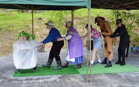 Pokaż zdjęcie: Program artystyczny w wykonaniu podopiecznych Stowarzyszenia "Nasz Dom". Podopieczni stoją na scenie w barwnych strojach