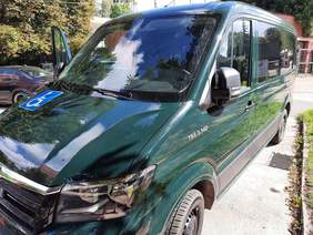 Pokaż zdjęcie: Na parkingu stoi zielony samochód przystosowany do przewozu osoby z niepełnosprawnością. 