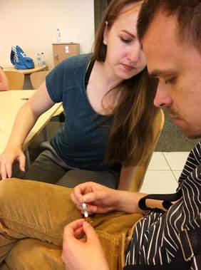 Pokaż zdjęcie: Podopieczny trzyma w ręku wykonany kolczyk, obok siedzi terapeuta