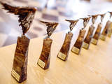 Złote statuetki ustawione w szeregu na jasno brązowym stole