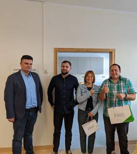 Pokaż zdjęcie: Na zdjęciu znajduje się trzech mężczyzn i jedna kobieta. kobieta i mężczyzna trzymają torbę z upominkami.