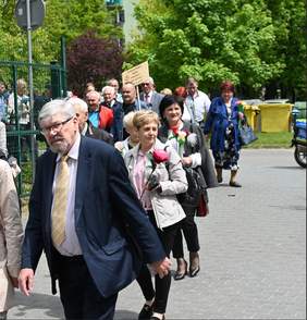 Pokaż zdjęcie: Ulicą idzie tłum ludzi. Na początku kroczy dyrektor Łódzkiego Oddziału PFRON. Za nim idą kobiety i mężczyźni. Wszyscy są ubrani na kolorowo. Niektórzy niosą kwiaty i transparenty. 