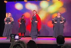 Pokaż zdjęcie: Ubrane w czarno-czerwone stroje ludowe kobiety, tańczą i śpiewają na scenie