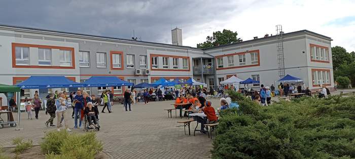 Pokaż zdjęcie: Na placu, gdzie odbywal się Pikinik stoją rozłone stoiska z obslugującymi je osobami, a także jest sporo gości-uczestników spotkania zainteresowanych atrakcjami Pikniku