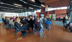 Pokaż zdjęcie: Sala pełna gości. Goście siedzą na krzesłach i słuchają przemawiających osób