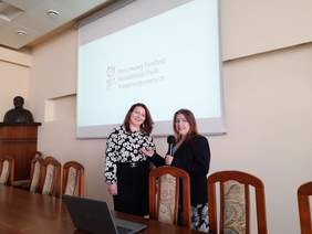 Pokaż zdjęcie: Za stołem stoją dwie kobiety, pozują do zdjęcia.