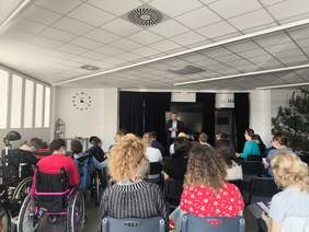 Pokaż zdjęcie: W sali zgromadziła się duża grupa młodzieży, w tym część osób na wózkach, przed młodzieżą stoi dwóch prelegentów.