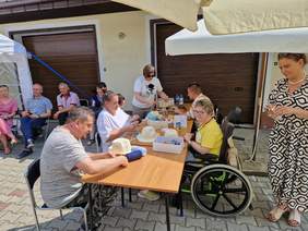 Pod parasolami grupa ok 10 osób w tym osoby na wózkach inwalidzkich, częścćozdabia kapelusze